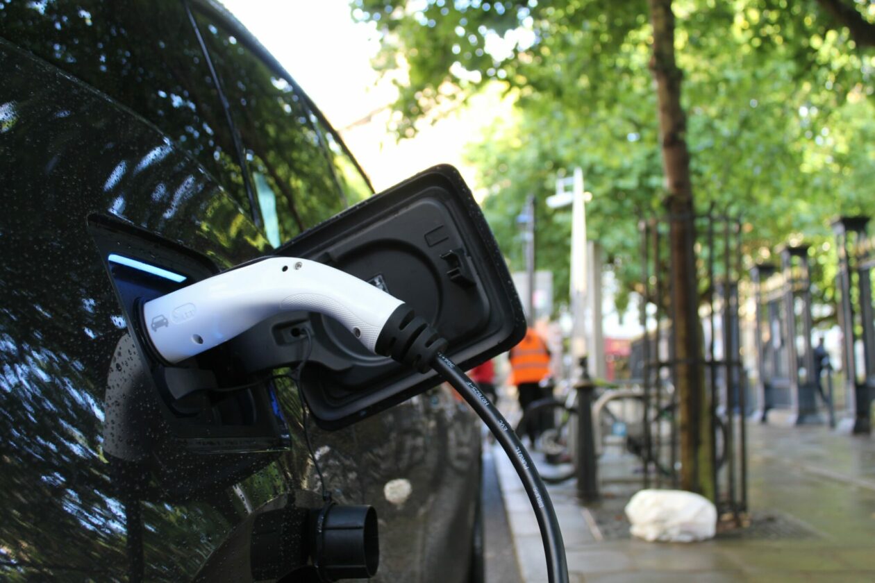 Photo of electric vehicle being charged on a tree-lined street