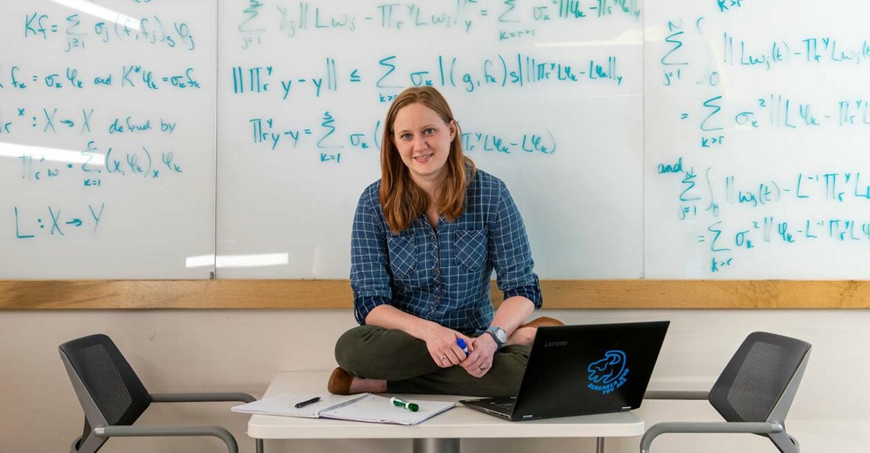 Student sitting on a table with a whiteboard behind her full of equations