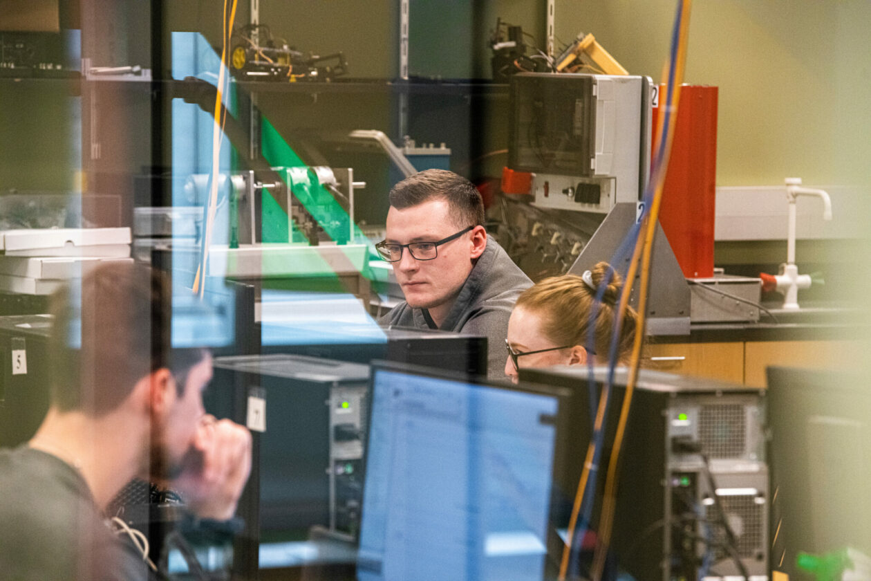 students at computers photographed through window with a slight reflection