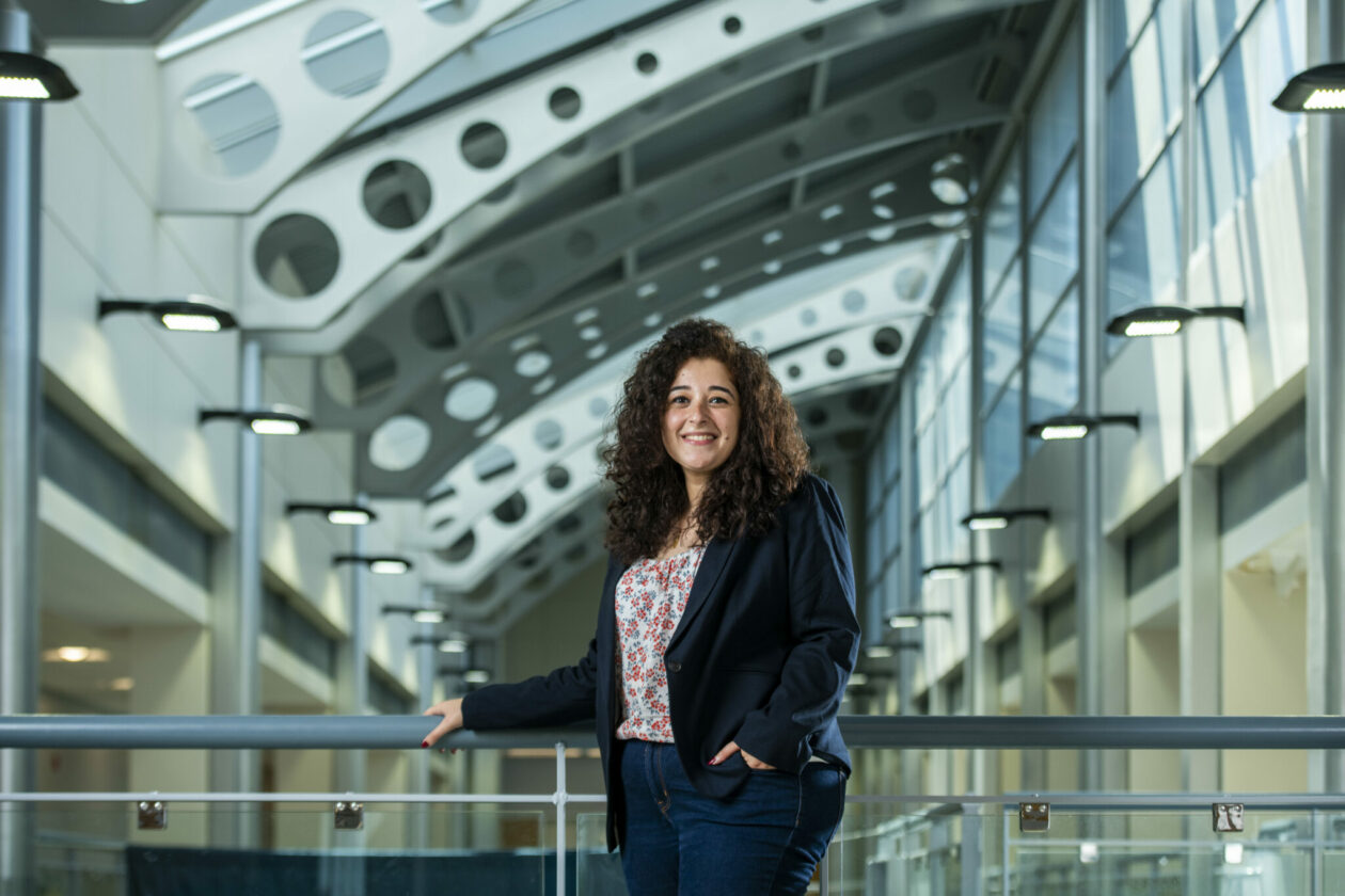 Young smiling woman wearing black pants and jacket with a light-colored top, standing in a building atrium