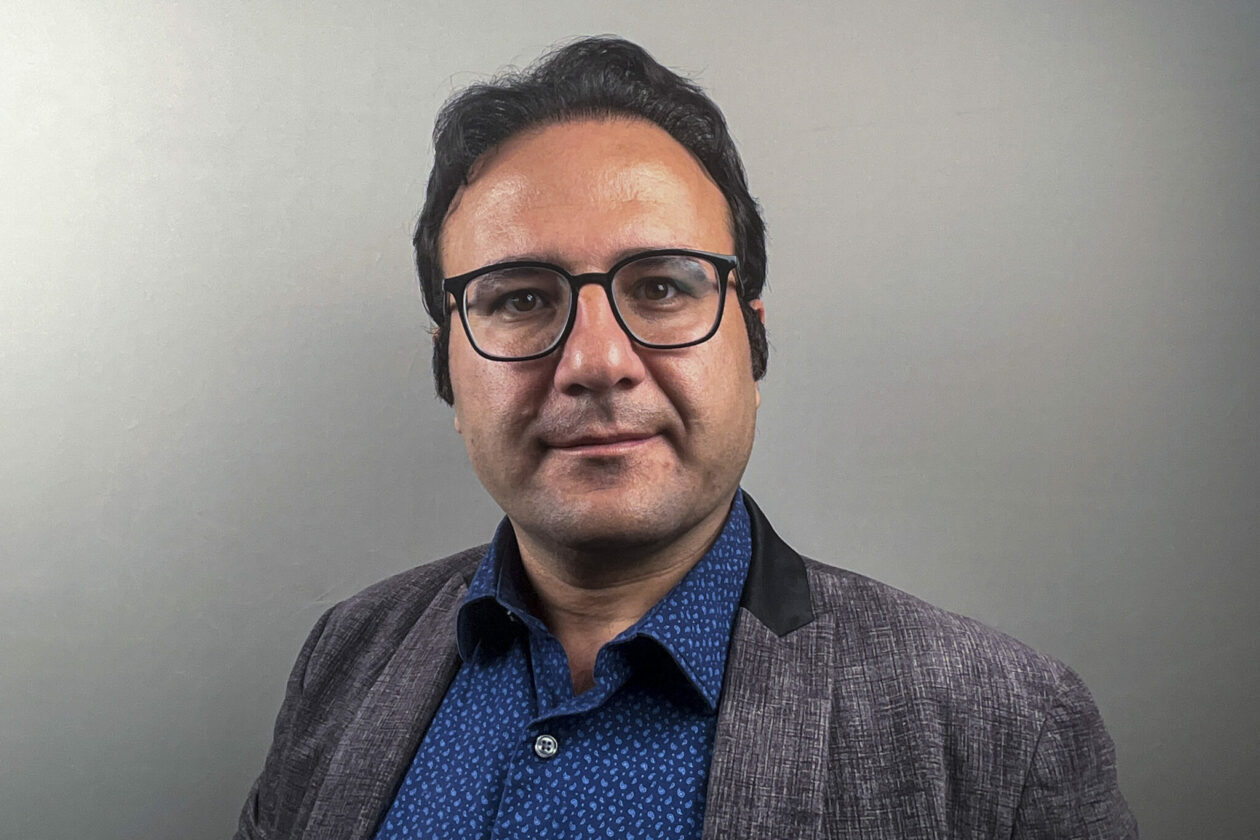 Portrait of man with short dark hair, wearing glasses, a blue shirt and gray jacket