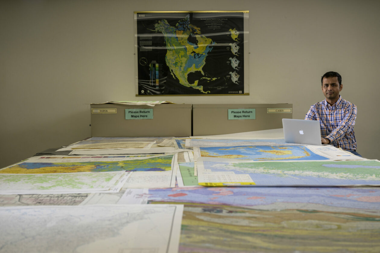 Dr. Satish Puri, an associate professor of computer science at Missouri S&T, poses with stacks of printed maps in the Curtis Laws Wilson Library that only represent a small fraction of the petabytes of digital data used for his research. Photo by Michael Pierce/Missouri S&T.