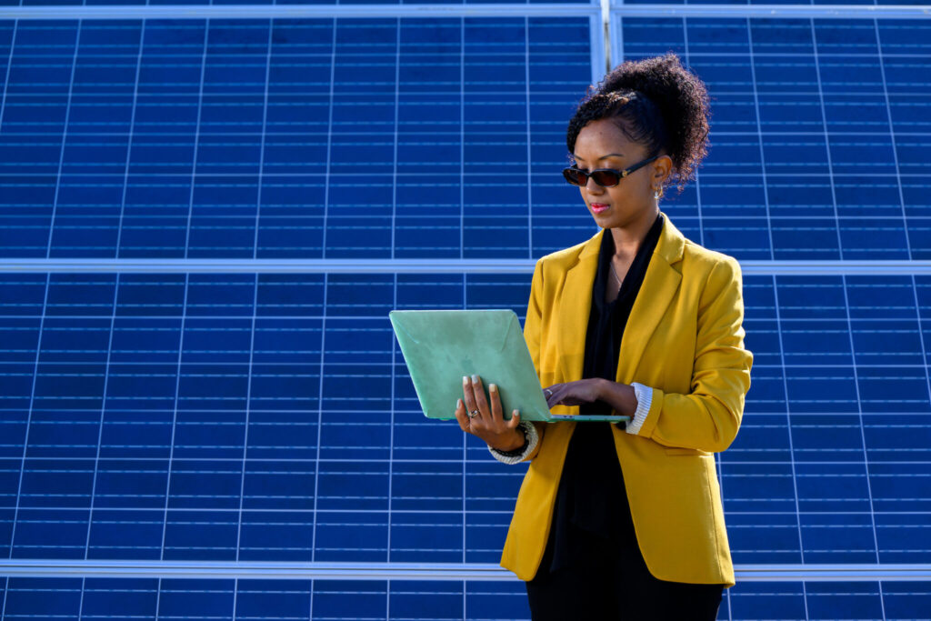 Mahelet Fikru holds laptop in front of solar panel.