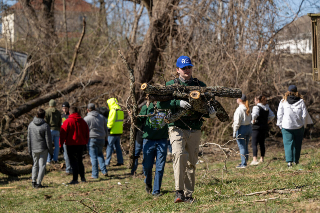 Individuals outdoors at site hit by tornado. S&T student carries tree branches in foreground.