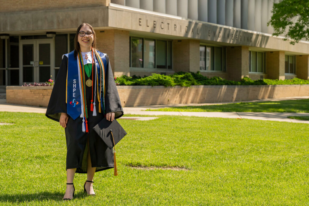 Woman in graduation regalia outside Emerson Hall. 