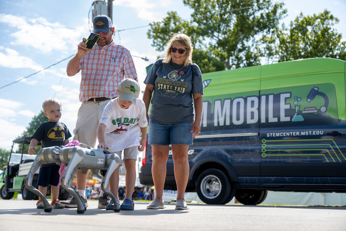 Two adults and two children with robot, STEM Mobile vehicle in background