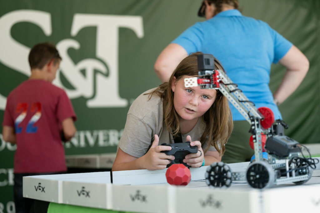 Girl with remote control operates robot, S&T signage in background