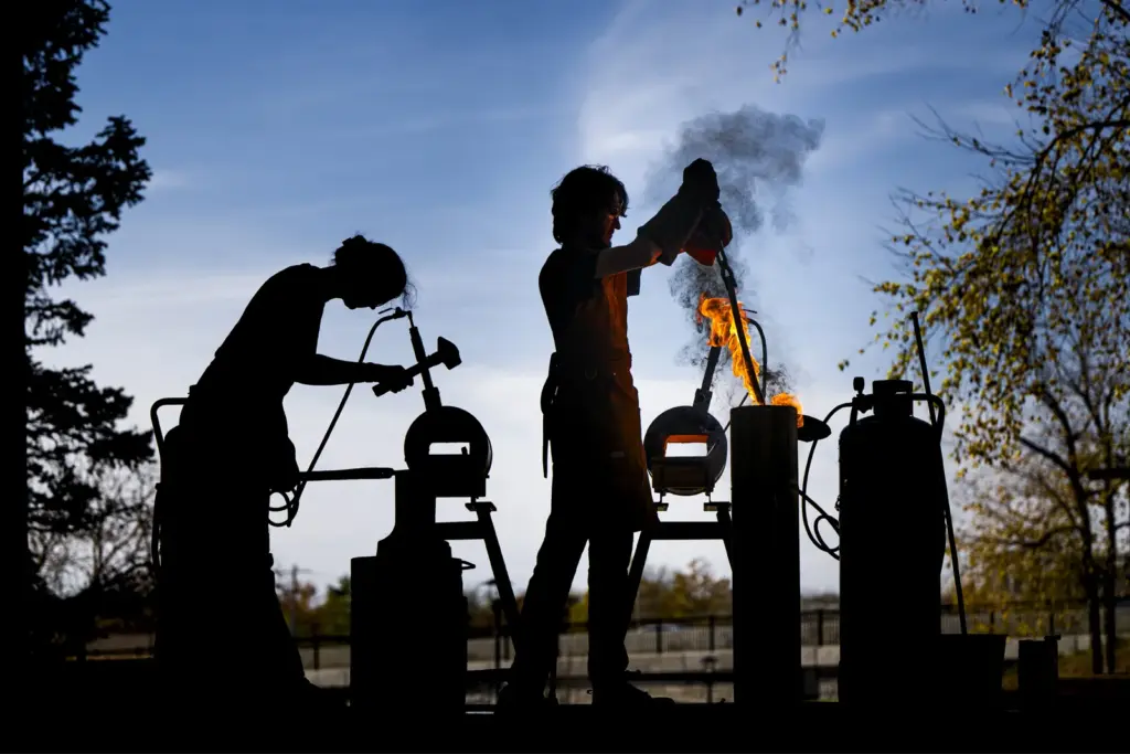 Profile of two students doing blacksmithing work outdoors