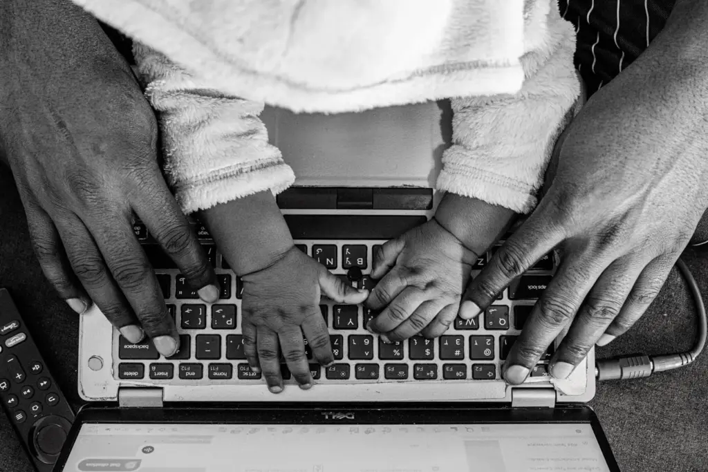 Black and white photo of adult and toddler hands on keyboard