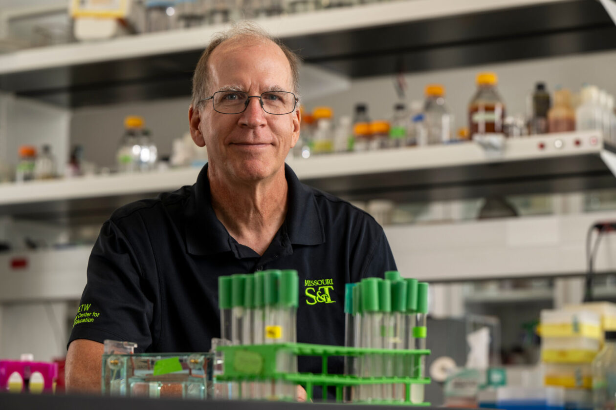 Male scientist sits in lab with test tubes in foreground
