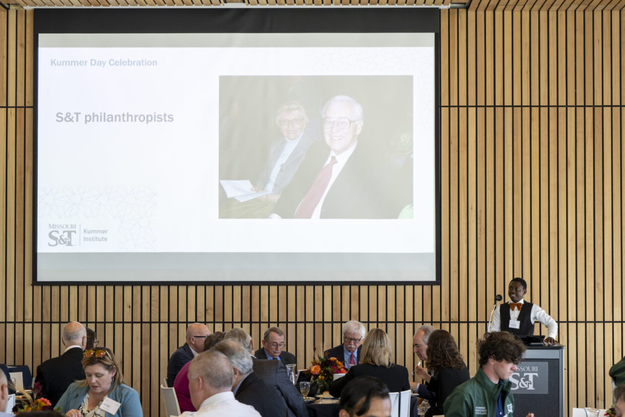 A student is speaking to the crowd in front of a presentation showing Fred and June Kummer, at the Innovation Lab forum.